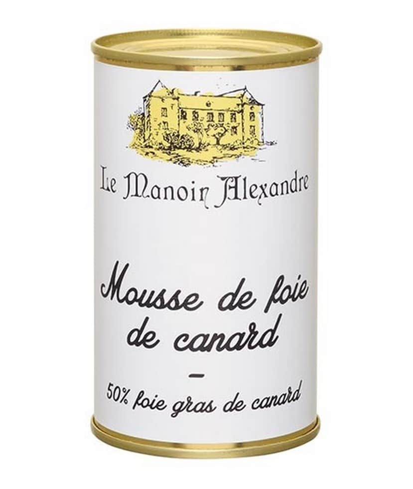 Burken med Manoir Alexandre Mousse de Canard au Foie Gras 190g, en större förpackning, visad på en träskiva med färska fikon och ett glas vin.