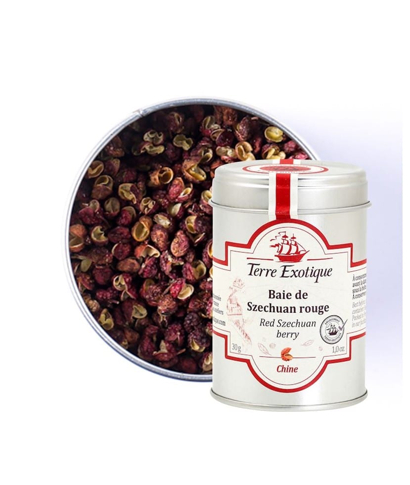 Burk med Terre Exotique Sichuanpeppar (30g). De röda och bruna pepparkornen (skalen) ligger på en sked bredvid en wokpanna, färsk ingefära och koriander, i en asiatisk köksmiljö.