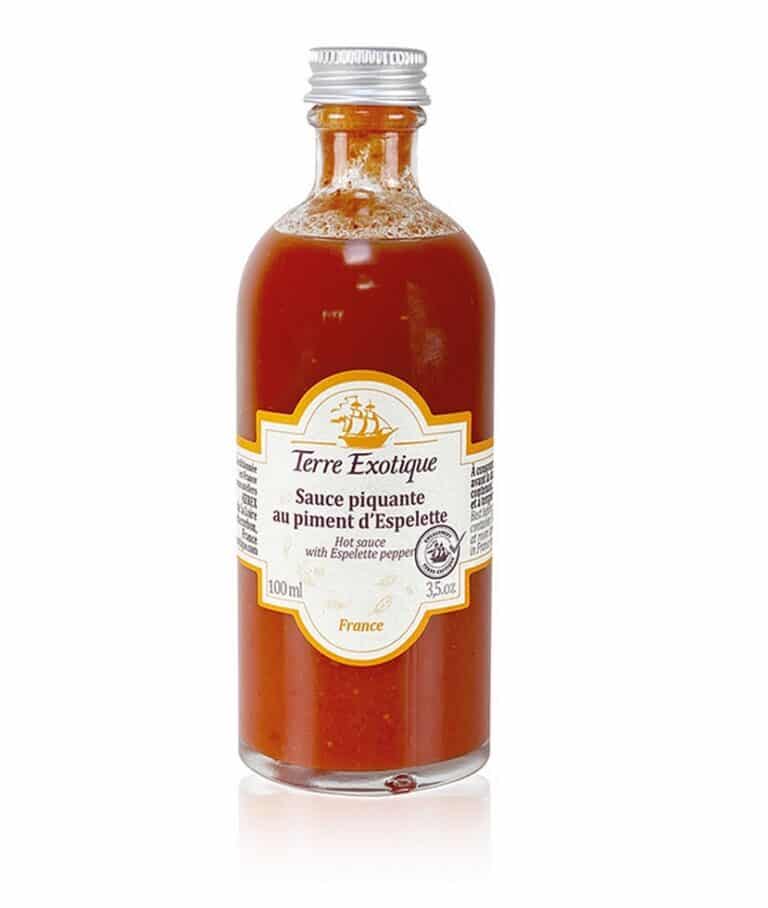 Liten glasflaska med Het sås baserad på Piment d'Espelette av märket Terre Exotique. Ljusorange sås med etikett.